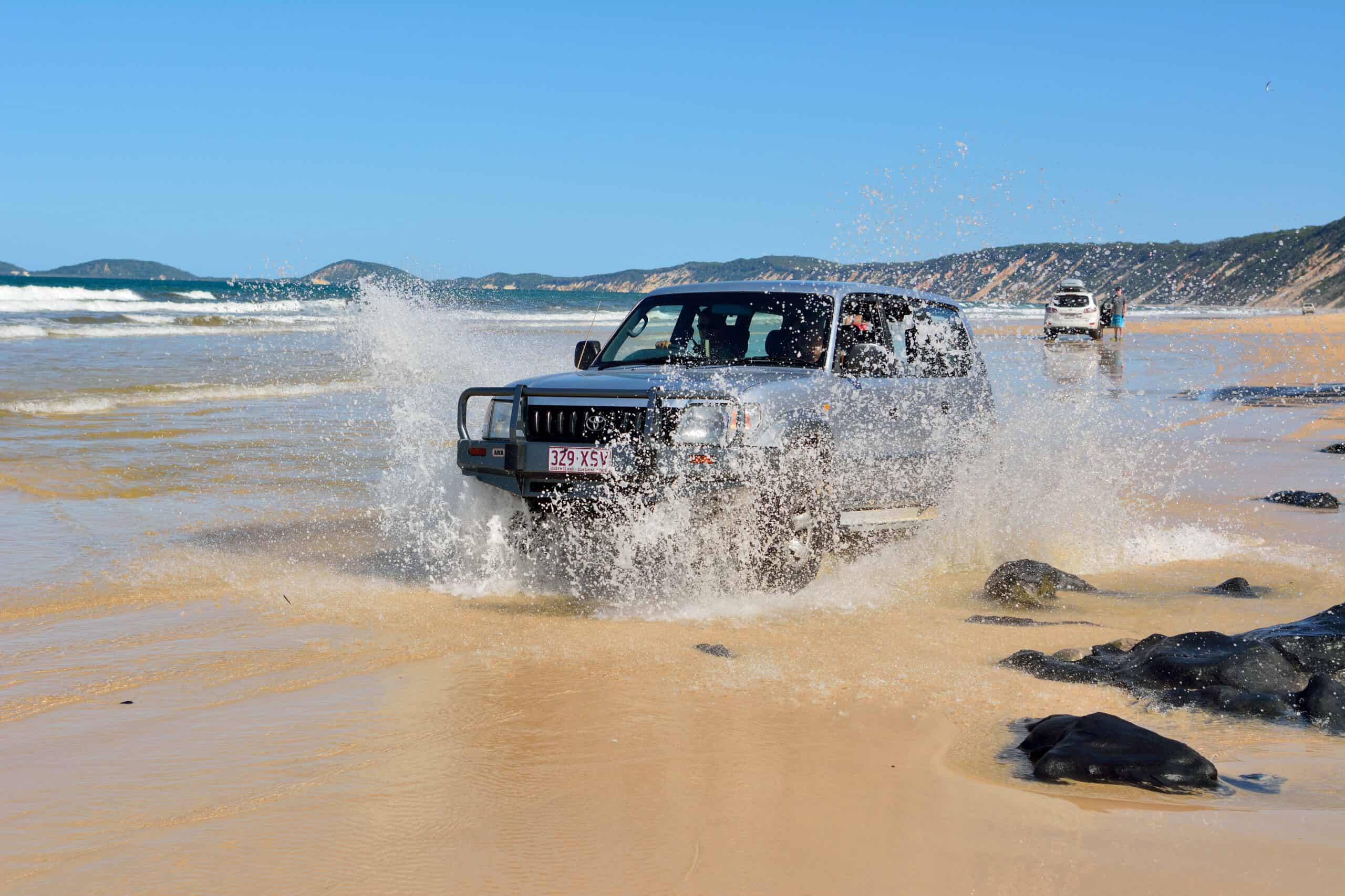 4WD vehicles driving along Rainbow Beach splashing through the sea.